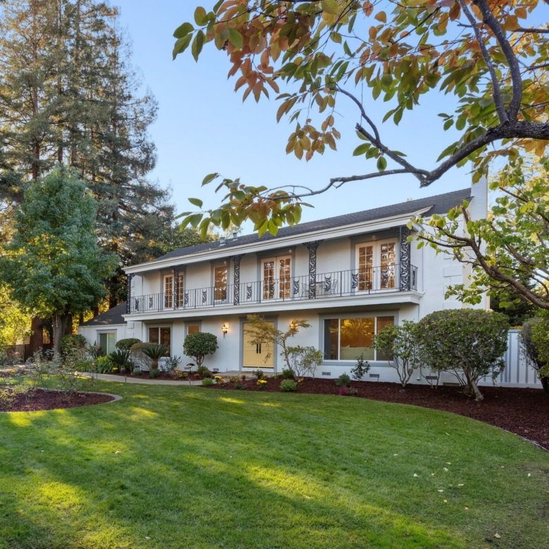 Two-story white estate with balcony and landscaped front lawn